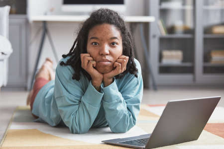 Portrait of real African American woman looking at camera while lying on floor in modern home...