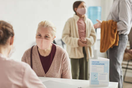 Portrait of white haired senior woman wearing mask while registering for covid vaccine at medical center, copy spaceの写真素材