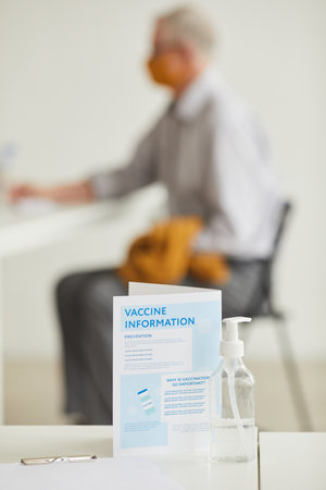 Vertical image of covid vaccination sign in clinic with senior man getting vaccine in background, copy spaceの写真素材