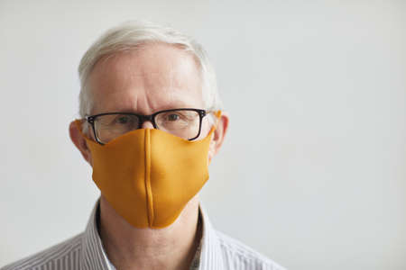 Close up portrait of white haired senior man wearing mask and looking at camera while standing against white background in clinic, copy spaceの写真素材