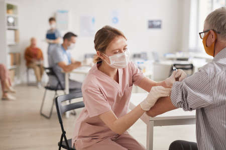 Portrait of young female doctor vaccinating senior man in vaccination center or medical clinic, copy...