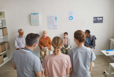 Back view portrait of group of doctors looking at patients waiting in line in vaccination center or clinic, copy spaceの写真素材