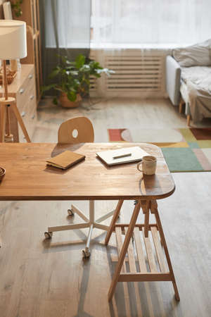 Vertical background image of cozy home office workplace with laptop on wooden desk scene lit by...