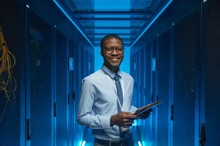 Waist up portrait of smiling African American man standing by server cabinet while working with...