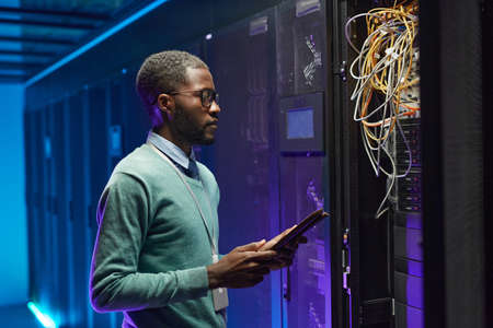 Side view portrait of African American data engineer holding digital tablet while working with...