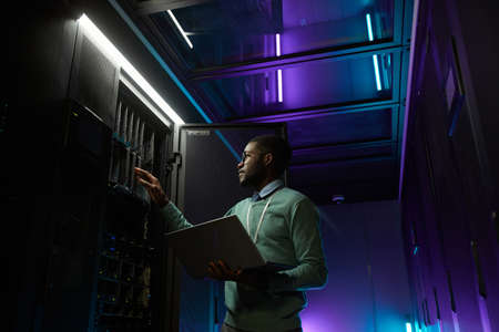 Low angle portrait of young African American data engineer working with supercomputer in server room...