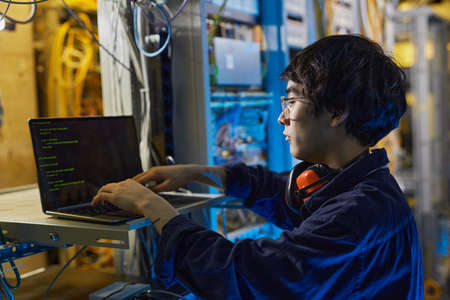 Side view portrait of young network technician using laptop while setting up internet connection in...