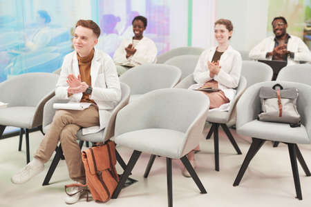 Full length portrait of multi-ethnic group of people applauding while sitting in audience and...