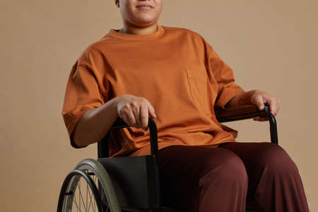 Cropped portrait of contemporary mixed race woman using wheelchair while posing in studio against...