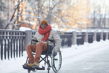 Full length portrait of African American man using wheelchair outdoors in winter and looking at camera , copy spaceの写真素材