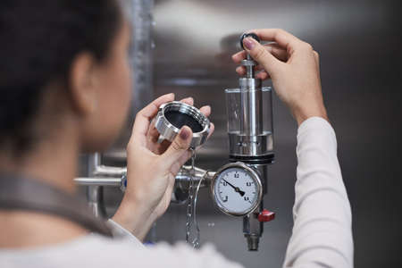 Back view close up of female worker checking pressure meter while operating machinery at industrial...