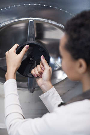 Vertical back view portrait of young female worker opening hatch at storage tank in industrial workshop, copy spaceの写真素材