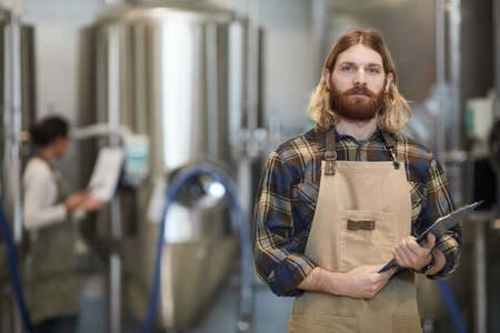 Waist up portrait of bearded man wearing apron posing in workshop of modern industrial brewery, copy spaceの写真素材
