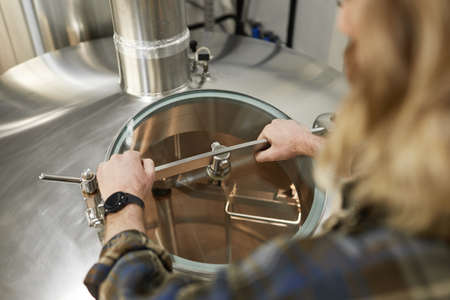 High angle close up of male worker opening tanks at brewery, beer making process, copy space