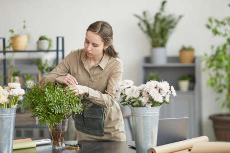 Portrait of young woman arranging flower compositions in green florists workshop, copy spaceの写真素材