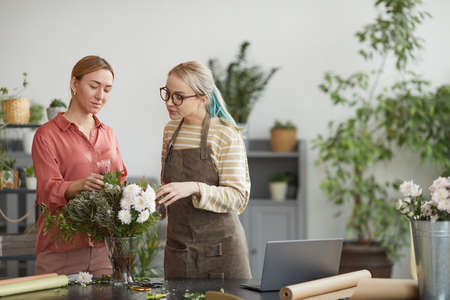 Waist up portrait of two young women arranging floral compositions while working in flower shop, copy spaceの写真素材