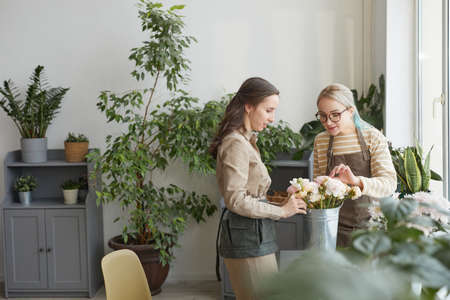 Minimal wide angle portrait of two young women arranging bouquets while enjoying work in florists studio, copy spaceの写真素材