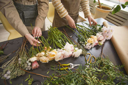 Close up of beautiful flowers on table in flower shop with two florists arranging bouquets, copy...