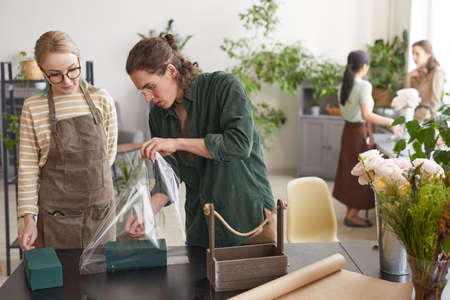 Portrait of young male florist arranging floral compositions in flower shop, copy spaceの写真素材