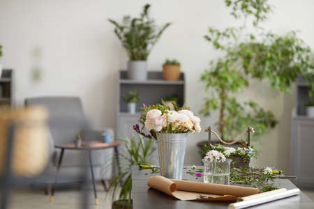 Background image of beautiful flowers in buckets and jars on table in florist workshop decorated by green plants, copy spaceの写真素材