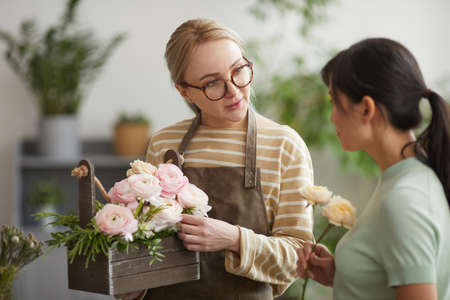 Waist up portrait of young woman giving bouquet to customer while working in flower shopの写真素材