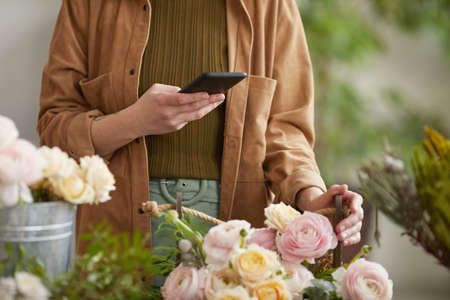 Close up of unrecognizable female florist taking photos of floral compositions via smartphone while working in flower shop, copy spaceの写真素材