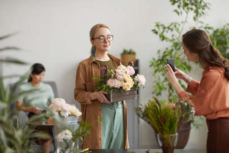 Portrait pf smiling female florist holding floral composition while posing for photo in flower shop, copy spaceの写真素材