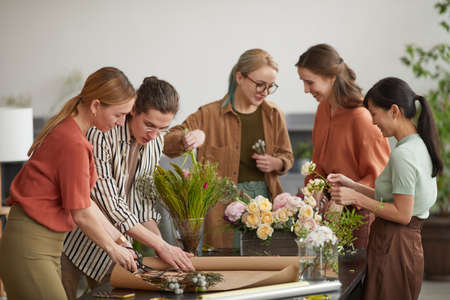 Diverse group of young florists arranging floral compositions while working in flower shopの写真素材