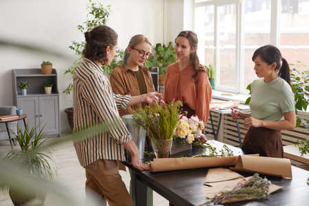 Wide angle view at diverse group of young florists arranging floral compositions while working in flower shopの写真素材