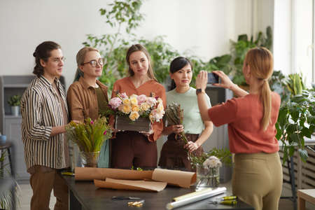 Diverse group of young florists florist holding floral composition while posing for photo in flower shopの写真素材
