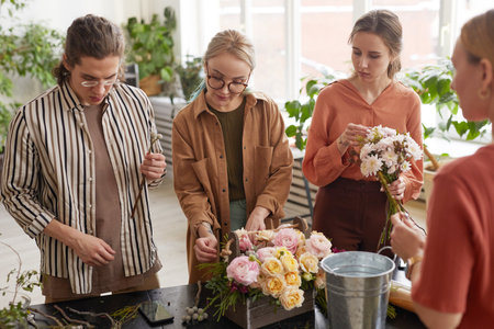 Diverse group of young people arranging flowers in florists workshop while attending class on floral artの写真素材