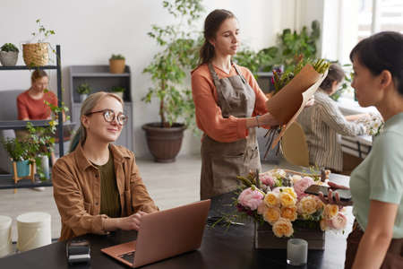 Portrait of two young female florists consulting customers while working in flower shop, copy spaceの写真素材