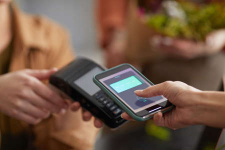 Close up of unrecognizable young woman paying via NFC in flower shop and buying bouquet , copy spaceの写真素材