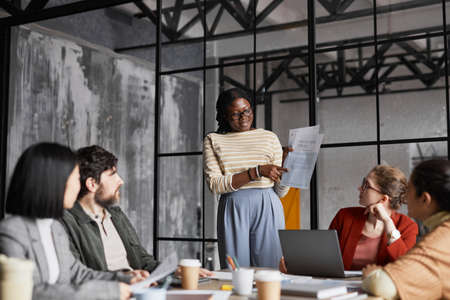 Portrait of smiling African-American woman giving presentation to colleagues during meeting in office, copy spaceの写真素材