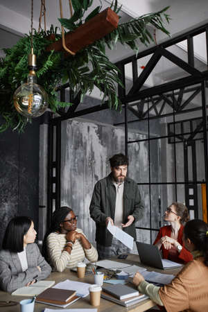 Vertical portrait of bearded businessman giving presentation to colleagues during meeting in office,...