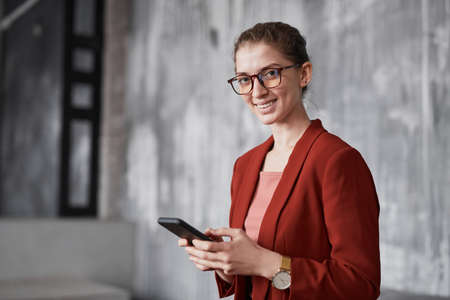 Portrait of smiling businesswoman wearing red while standing against grey wall in office, copy spaceの写真素材