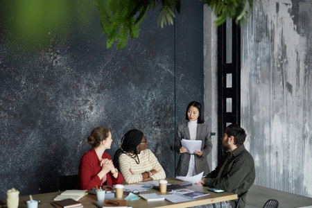 Highh angle portrait of young Asian businesswoman talking to group of colleagues during meeting at...