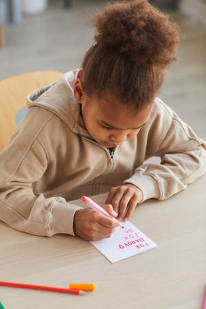 Vertical portrait of cute African-American girl making handmade card as gift for Fathers day, copy...