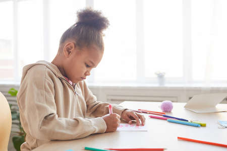 Side view view portrait of cute African-American girl signing handmade card as gift for Fathers day, copy spaceの写真素材
