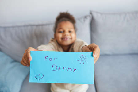 High angle close up of smiling African-American girl holding letter for dad to camera on Fathers day, copy spaceの写真素材