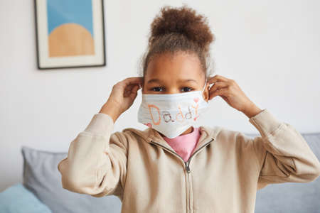 Front view portrait of cute African-American girl wearing mask at home on Fathers day and looking at camera, copy spaceの写真素材