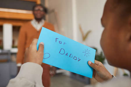 Close up of mixed-race little boy holding letter for dad while giving handmade present on Fathers day, copy spaceの写真素材