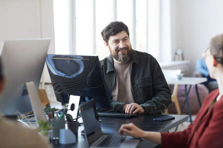 Portrait of smiling bearded man talking to colleagues during meeting in modern IT office, copy space