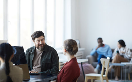 Portrait of smiling bearded man talking to female colleague during meeting in modern office, copy...