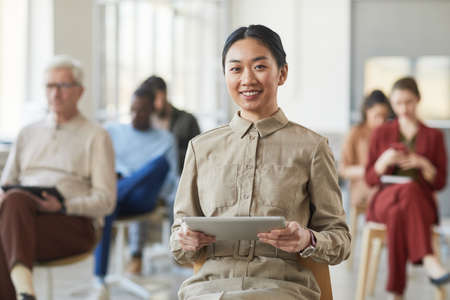 Portrait of successful Asian businesswoman smiling at camera while posing in office with people in...