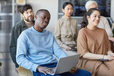 Diverse group of business people sitting on chairs in audience and listening at meeting or seminar,...