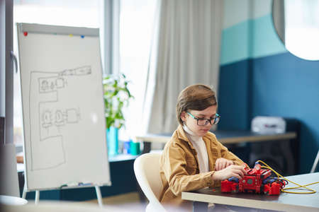 Side view portrait of cute boy building robotic machine while enjoying engineering class in...