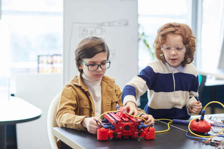 Portrait of two boys building robot together while enjoying engineering class in development school,...
