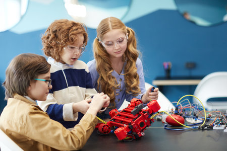 Portrait of three cute children building robot together while enjoying engineering class in...
