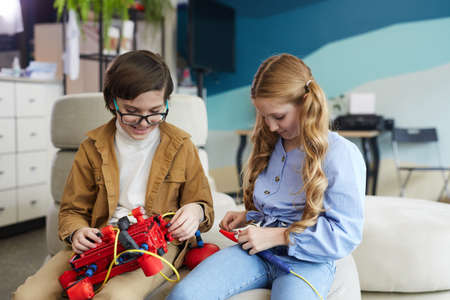 Portrait of two children playing with robot machine during engineering class in modern school interior, copy spaceの写真素材